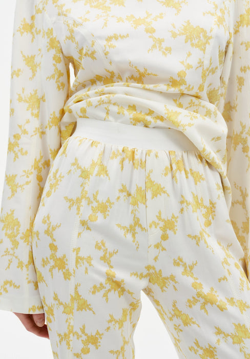 Close-up of cream trousers with a yellow abstract floral print, featuring a high elasticated waistband and soft draping fabric, paired with a matching long-sleeve top.