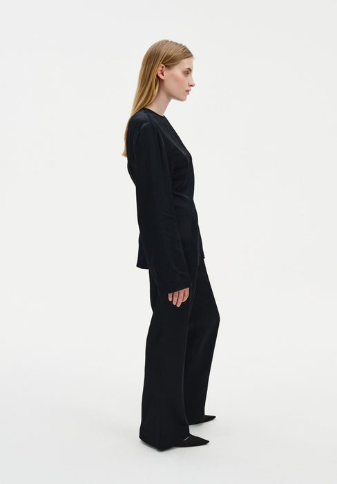 Side profile of a woman wearing a black long-sleeve top and matching wide-leg trousers, highlighting the clean lines and tailored fit of the outfit against a plain studio background.