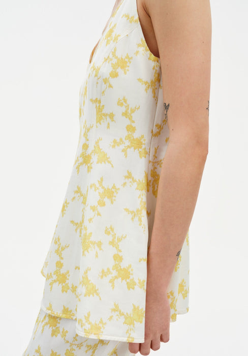 A close-up side view of a woman’s torso and arm, showing a relaxed posture with subtle tattoos on her arm against a plain background.