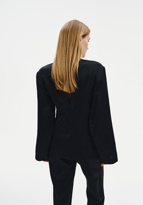 A woman with straight blonde hair is shown from the back in a relaxed standing pose against a plain background, her head slightly turned to the side.