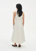 Back view of a model wearing a sleeveless cream midi dress with a clean A-line silhouette and racer-style back, paired with black low heels.