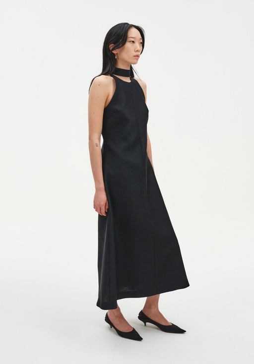 Three-quarter side view of a sleeveless black midi dress with a choker-style neckline and fluid A-line shape, paired with black low heels.