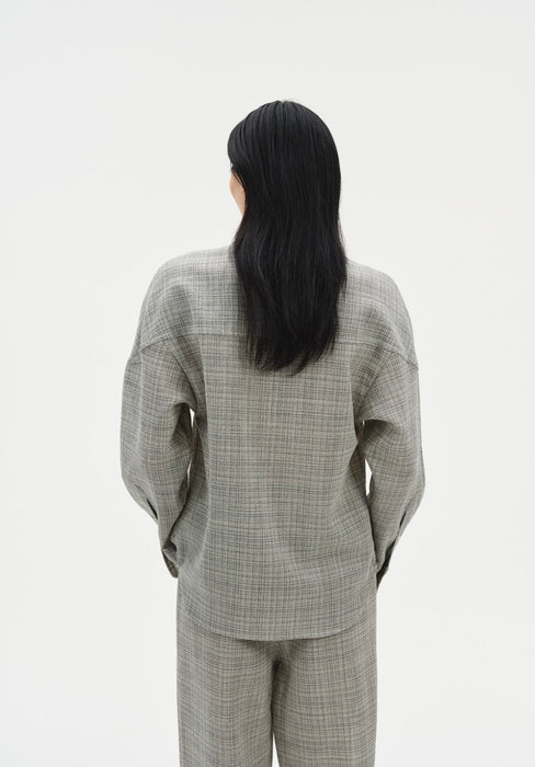 Back view of a woman standing upright with a relaxed posture, her hair falling straight down her back, facing away from the camera against a plain studio background.
