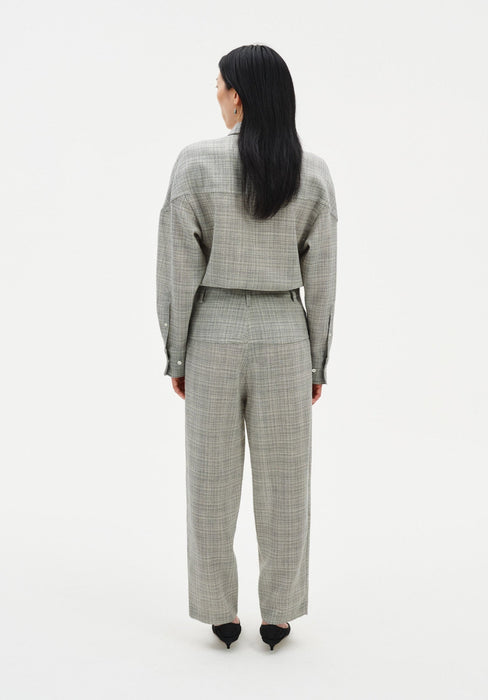 Full-length back view of a woman wearing a grey textured cropped jacket with matching high-waisted trousers, featuring a relaxed straight-leg fit, paired with black pointed heels in a minimalist studio setting.