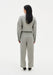 Full-length back view of a woman wearing a grey textured cropped jacket with matching high-waisted trousers, featuring a relaxed straight-leg fit, paired with black pointed heels in a minimalist studio setting.