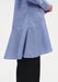 Close-up of a light blue long-sleeve tunic with fine vertical stripes, highlighting a curved seam and flared hem detail, worn over black wide-leg trousers.