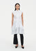 Front view of a model wearing a sleeveless white button-down tunic with a pointed collar and layered flared hem, styled over black slim trousers and paired with black pointed heels.