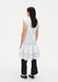 Back view of a model wearing a sleeveless white tunic with a structured fit and tiered ruffled hem, styled over black cropped trousers and paired with black pointed heels.