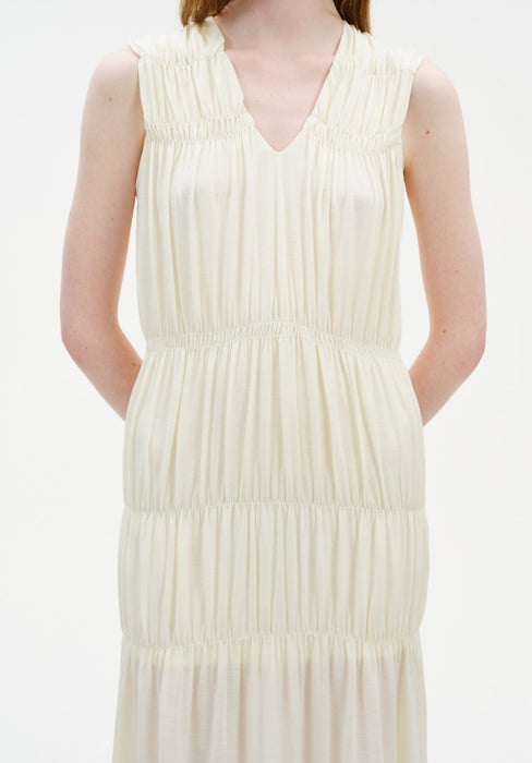 Close-up of a sleeveless cream-colored dress showing a V-neckline and gathered detailing at the shoulders, waist, and tiers, creating a soft, textured, and flowing silhouette.